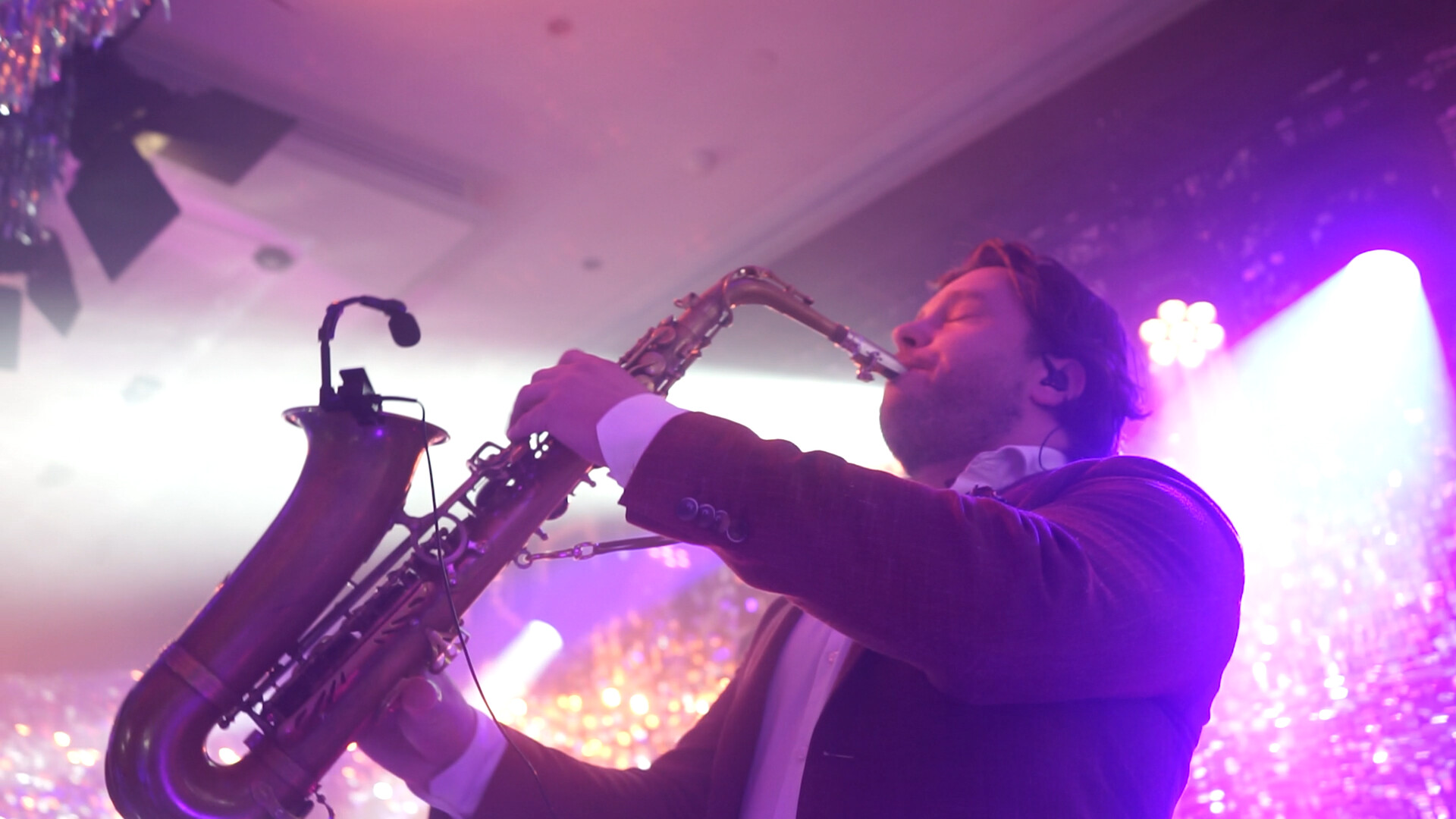 Saxophonist performing live under violet stage lights.